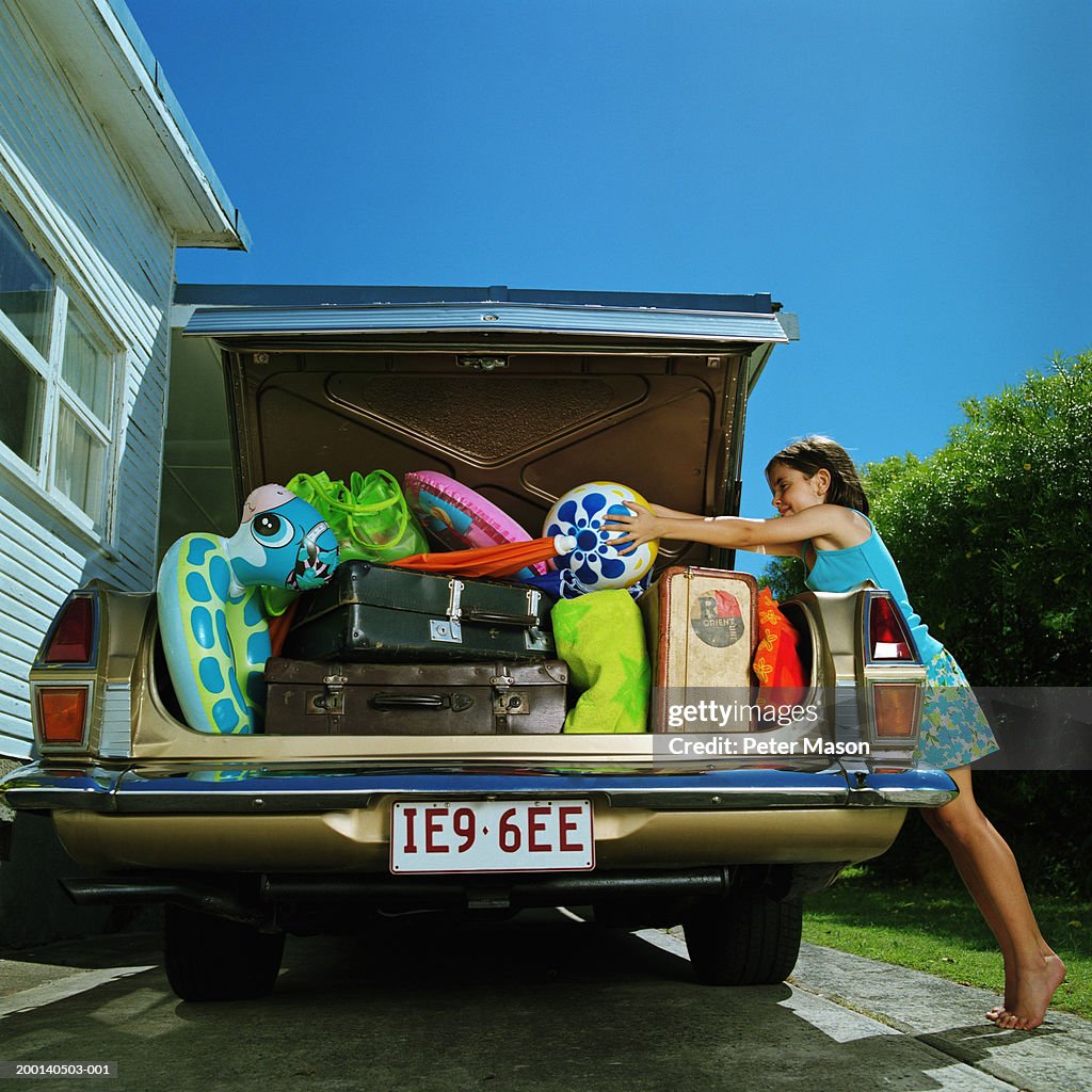 Girl (6-8) placing ball in heavilly loaded car boot