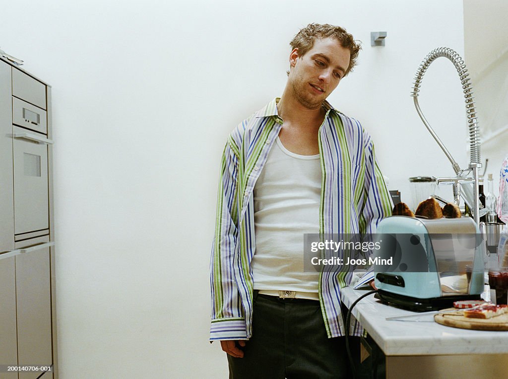 Man standing in kitchen, looking at burnt toast in toaster