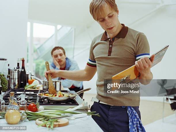 two men in kitchen, one preparing vegetables in frying pan - kochbuch stock-fotos und bilder