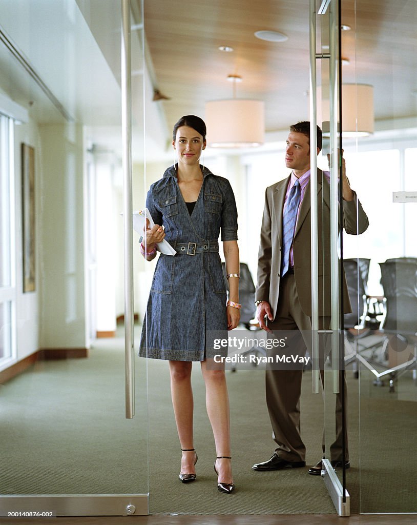 Businessman holding conference room door for businesswoman