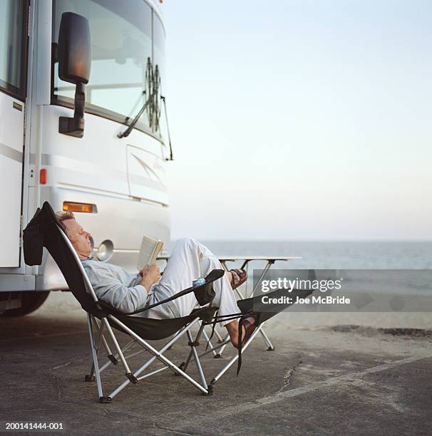 man sitting in chairs reading, rv camping at beach - campingstuhl stock-fotos und bilder