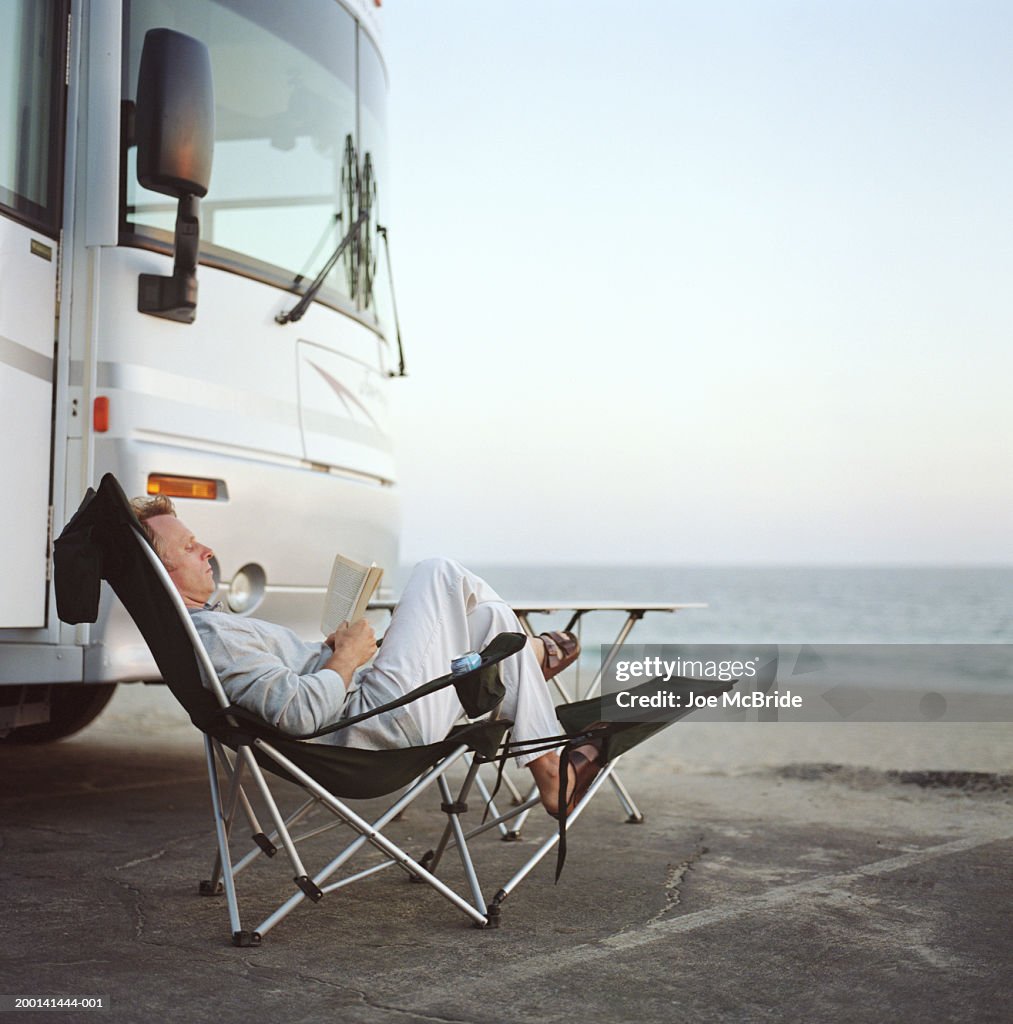 Man sitting in chairs reading, RV camping at beach