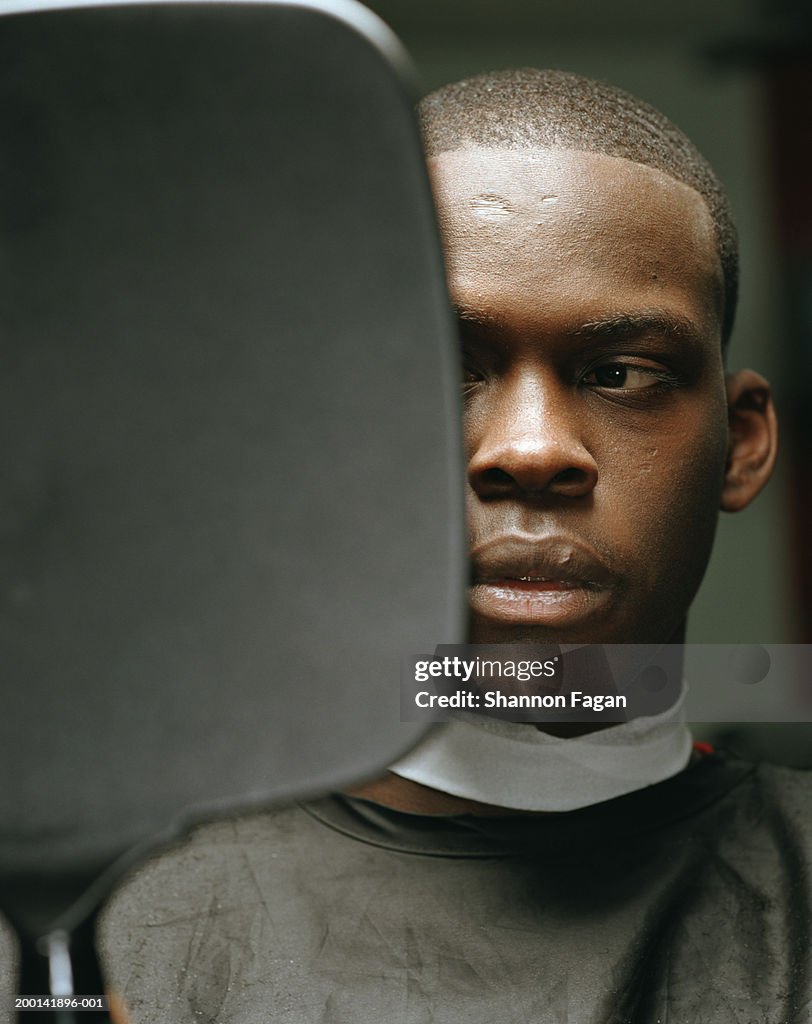 Man in barber's chair, looking in handheld mirror