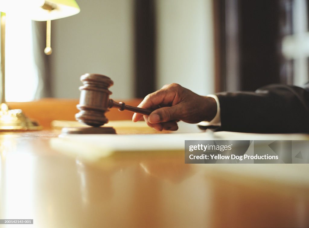 Male judge striking gavel in courtroom, close-up