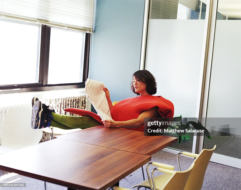 Young man wearing carrot costume in office, reading newspaper