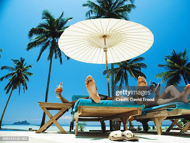 couple relaxing on sunloungers under parasol, low section - strand liegen stock-fotos und bilder