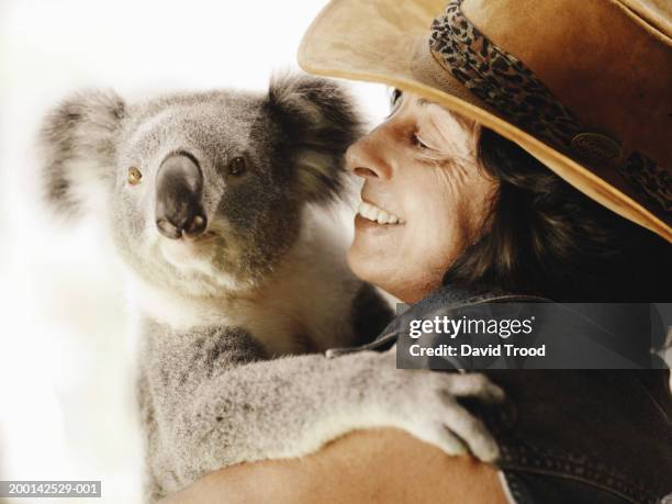 mature woman holding koala, close-up - akubra hat stock-fotos und bilder