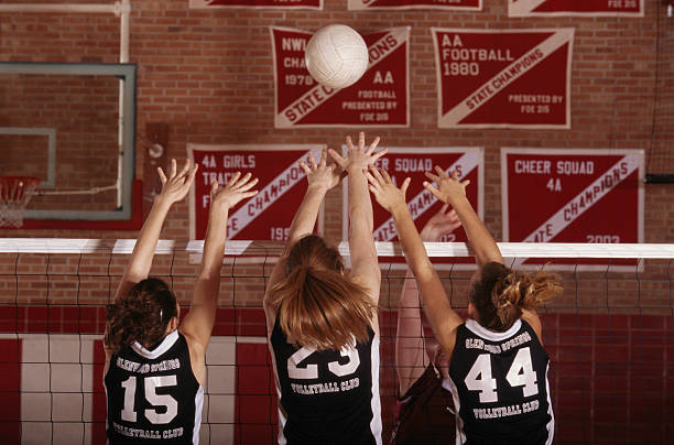 girls (14-16) volleyball players jumping to block ball at net - girls volleyball stock pictures, royalty-free photos & images