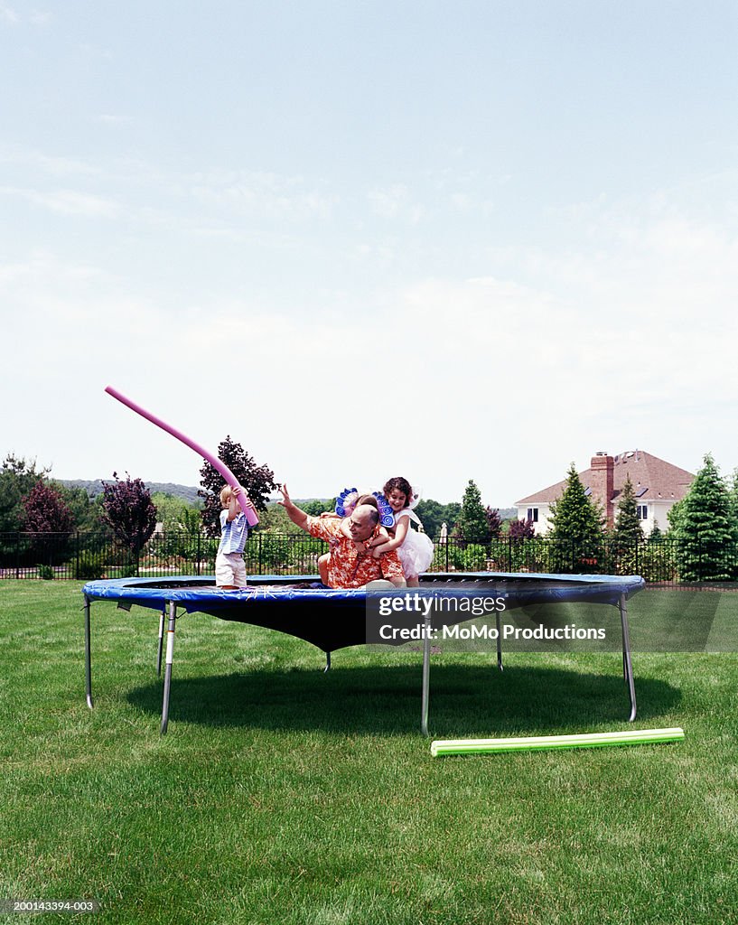 Father and children (2-8) playing on trampoline on lawn