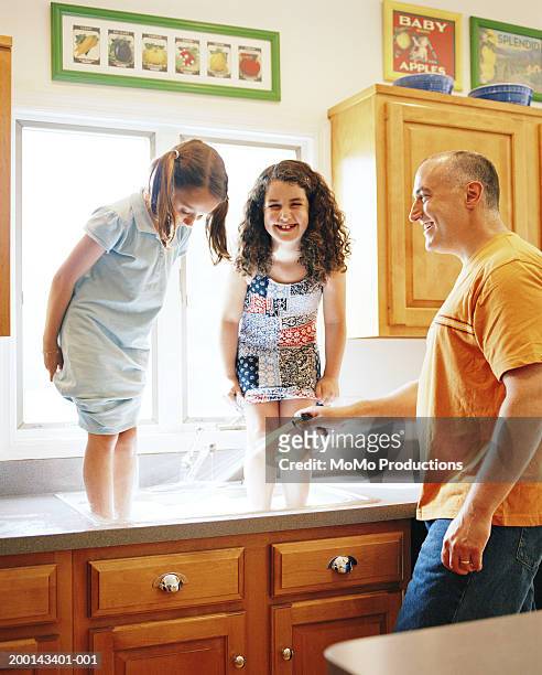girls (5-8) standing in kitchen sink, father hosing their feet - resourceful stock pictures, royalty-free photos & images