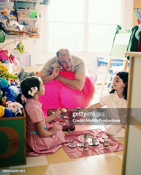girls (5-8) playing with toy tea set, father using mobile phone - indoor picnic stock pictures, royalty-free photos & images