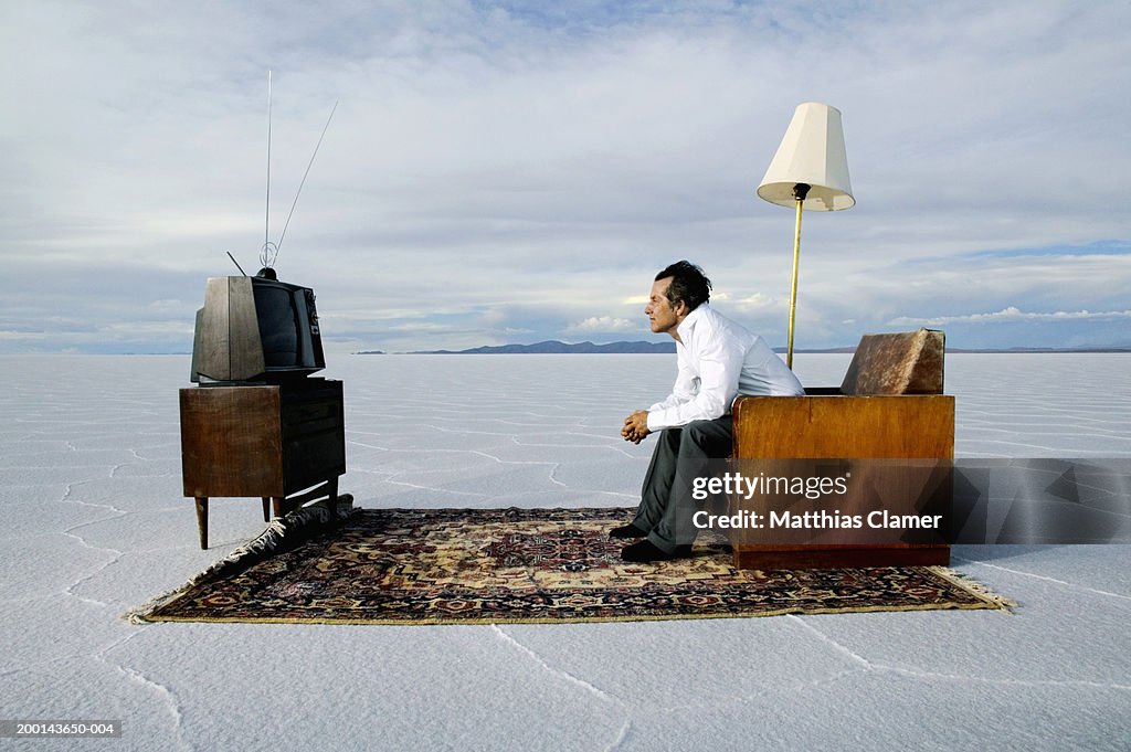 Mature man watching television on salt flat, side view