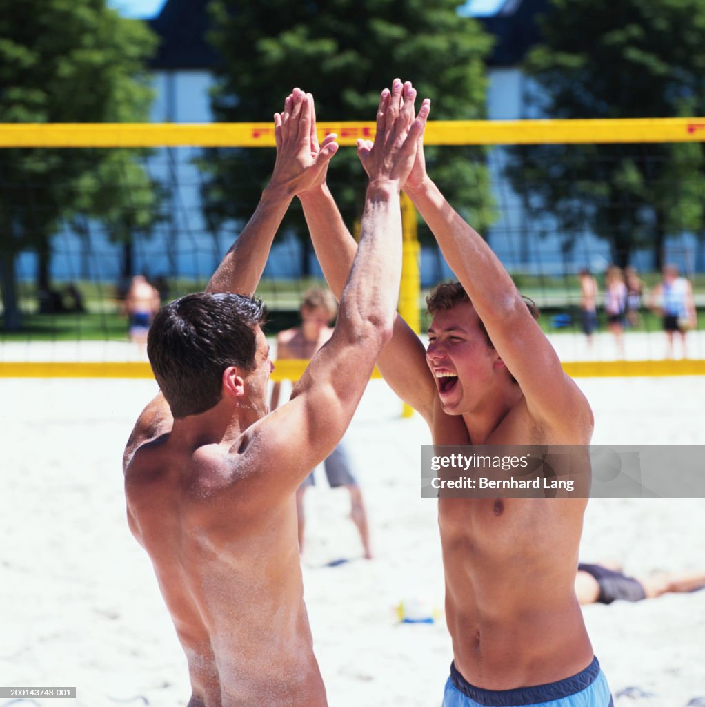 Two men joining hands above heads by beach volleyball net