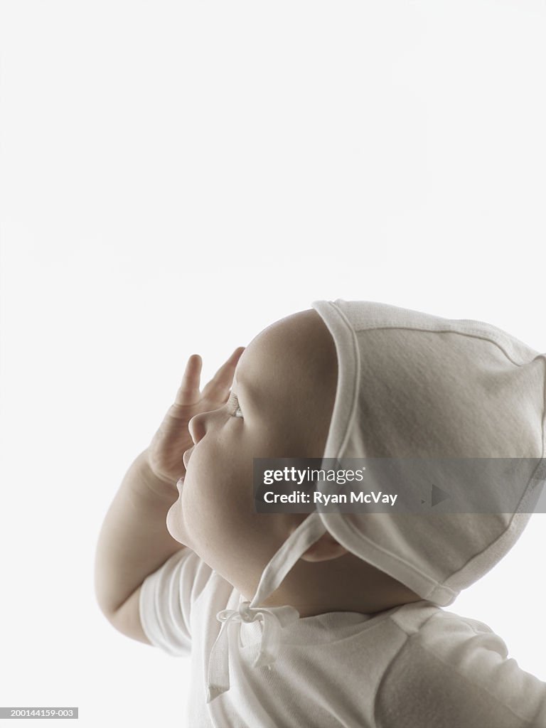 Baby Boy Wearing Bonnet Touching Face Side View High-Res Stock