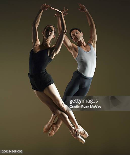 male and female ballet dancers in mid air pose, arms raised - ballerinas stock-fotos und bilder