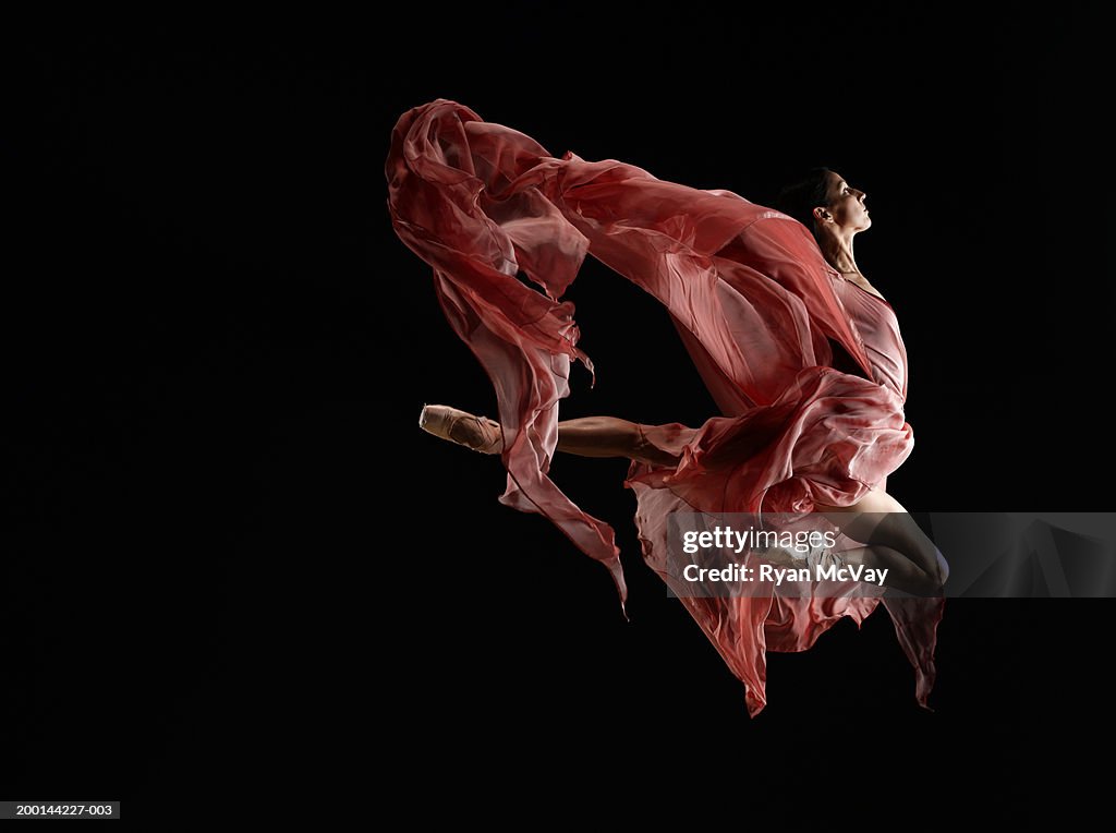 Ballet dancer wearing flowing dress in mid air leap, side view