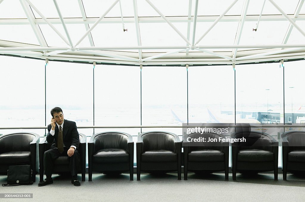 Businessman in airport waiting area using mobile phone