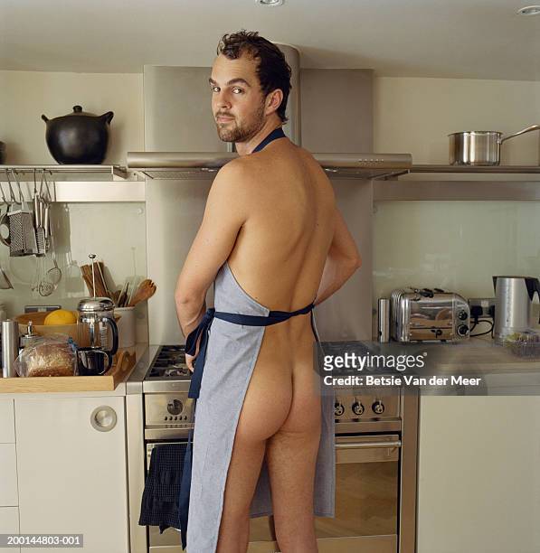 naked man wearing apron in kitchen, looking over shoulder, portrait - nudity foto e immagini stock