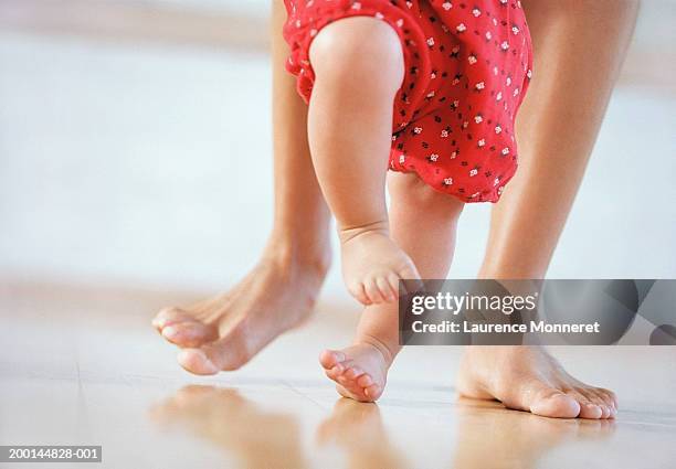 mother helping baby girl (9-12 months) to walk, low section - first occurrence stockfoto's en -beelden