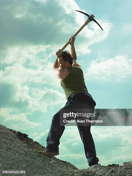 man swinging pick axe on mound of clay, low angle view - axe swing stock pictures, royalty-free photos & images