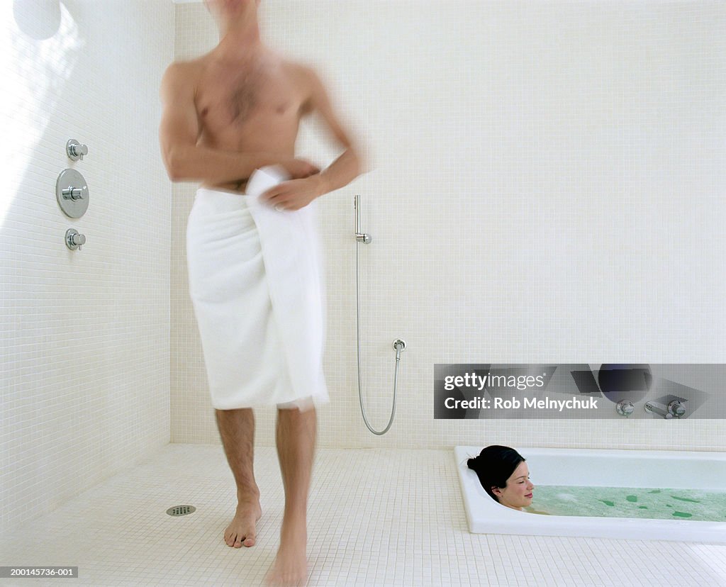 Man in towel walking past woman in bathtub (blurred motion)