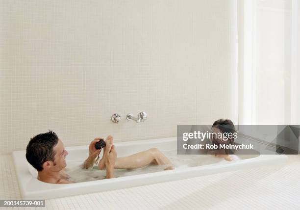 man scrubbing woman's foot with pumice stone in bubblebath - couple bathtub photos et images de collection