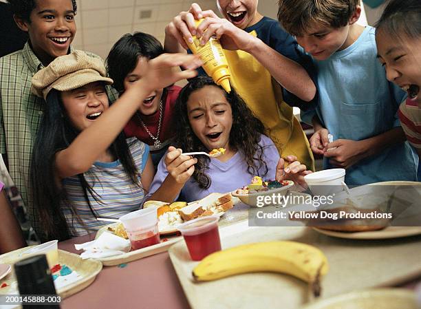 group of kids (12-14)        around table, boy pouring mustard in food - dog eats out girl stock-fotos und bilder
