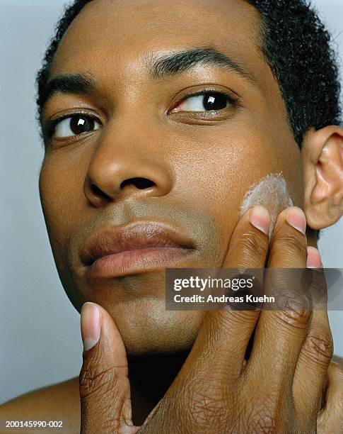 young man applying moisturizer to face, close-up - mann creme stock-fotos und bilder