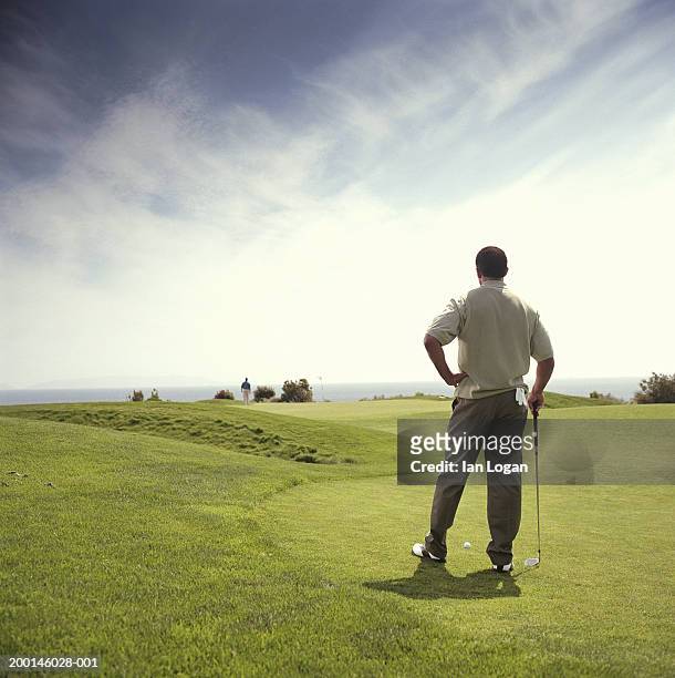 male golfer standing on green waiting to resume play, rear view - golf accessories stock pictures, royalty-free photos & images