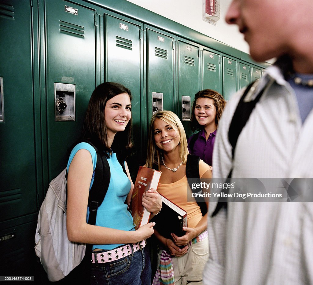 Teenage girls (16-18) standing near locker, looking at boy, smiling