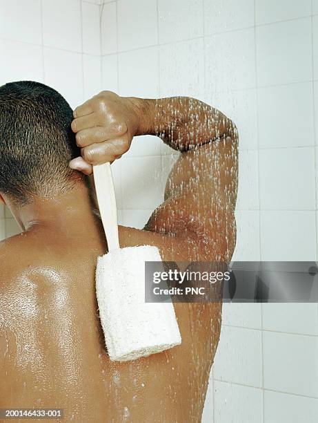 man scrubbing back with loofah in shower, rear view - hombre en la ducha fotografías e imágenes de stock