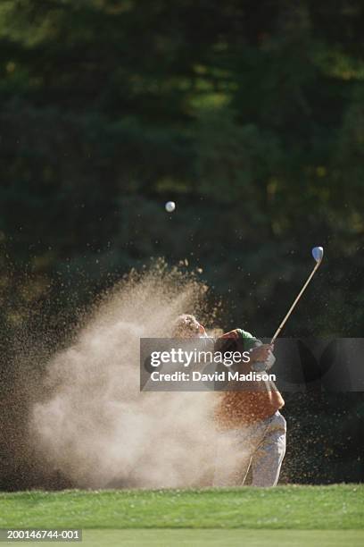 male golfer hitting out of a sand trap onto the green - golf bunker stock-fotos und bilder