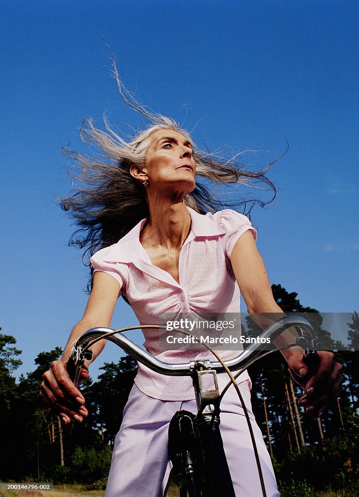 Mature woman riding bicycle, hair blowing in wind, low angle view