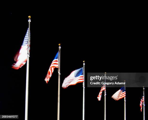 american flags blowing at the washington monument on a dark winter night - washington monument dc stock pictures, royalty-free photos & images