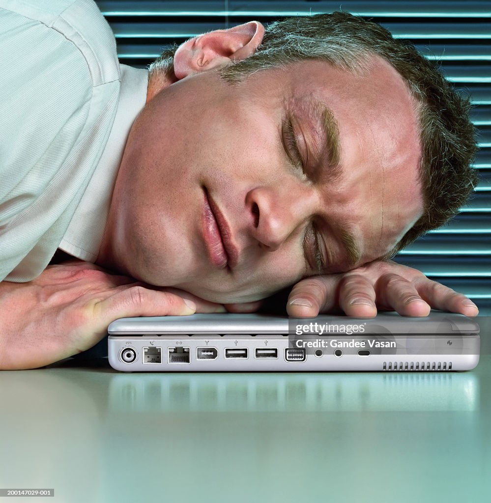 Man sleeping with head on closed laptop computer, close-up