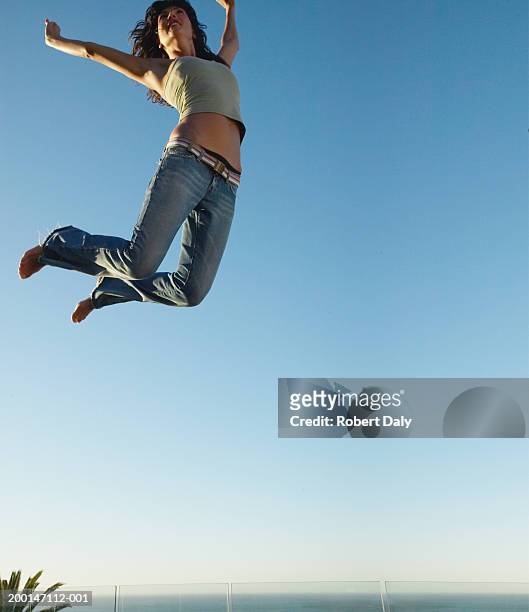 young woman jumping on trampoline, arms outstretched, low angle view - trampoline jump stock-fotos und bilder