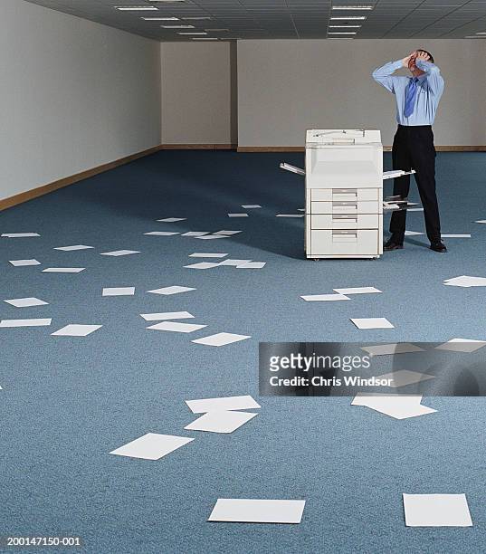 man in office by photocopier and scattered papers, hands on head - copier stock pictures, royalty-free photos & images