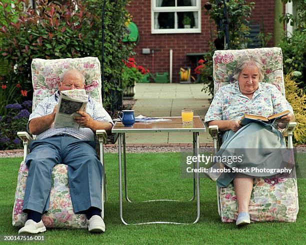 senior couple reading on adjacent garden chairs - vilfåtölj bildbanksfoton och bilder