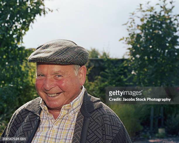 senior man wearing flat cap outdoors, smiling, portrait - chubby men stock-fotos und bilder