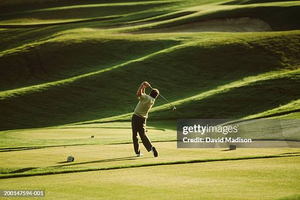 mature male golfer teeing off, rear view - afslag stockfoto's en -beelden