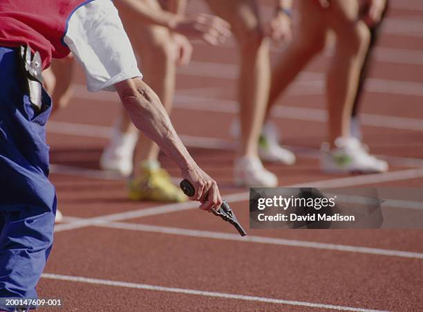 man holding starting gun, runners on starting line in background - starter gun photos et images de collection