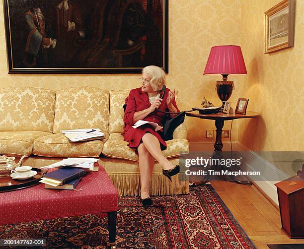 senior woman on sofa holding telephone receiver - stoneplus5 stock-fotos und bilder