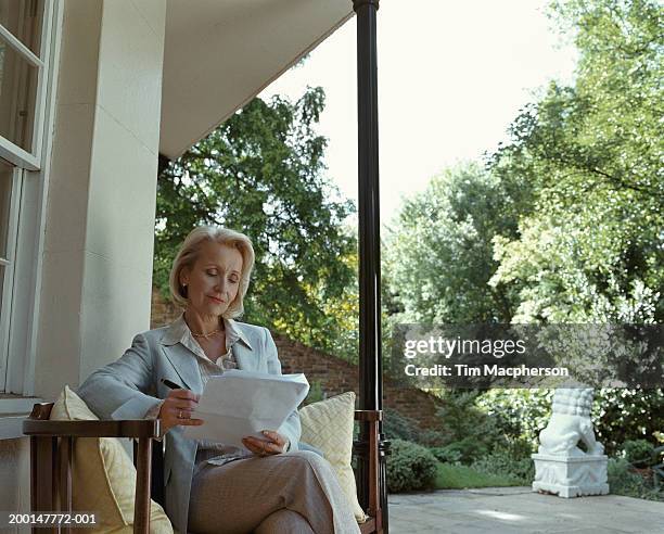 mature woman reading paperwork by patio window - stoneplus4 stock pictures, royalty-free photos & images