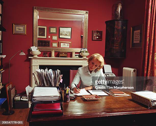 mature woman writing on paperwork at desk - stoneplus5 stock-fotos und bilder