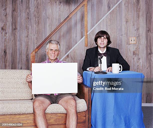 mature man holding blank sign on talk show in basement - family on couch with mugs stock-fotos und bilder