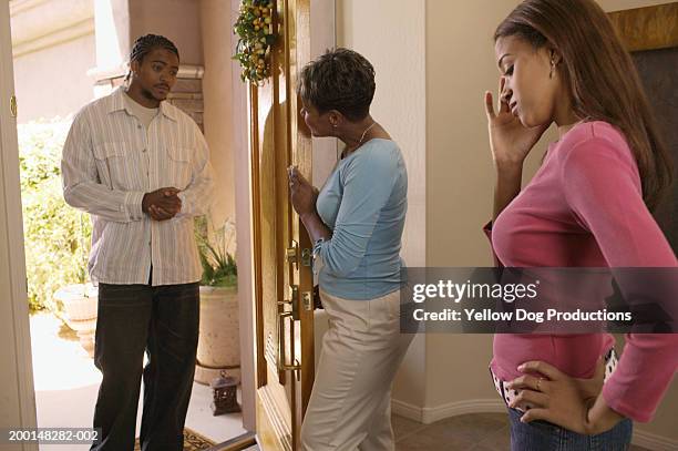mature woman answering door, daughter (16-18) looking downward - awkward date stock-fotos und bilder