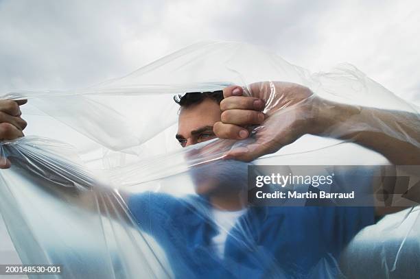 man tearing hole in transparent bag from inside, outdoors - break through fotografías e imágenes de stock