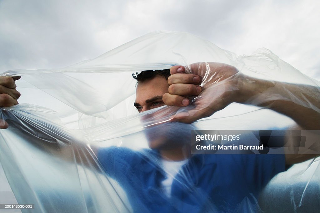 Man tearing hole in transparent bag from inside, outdoors