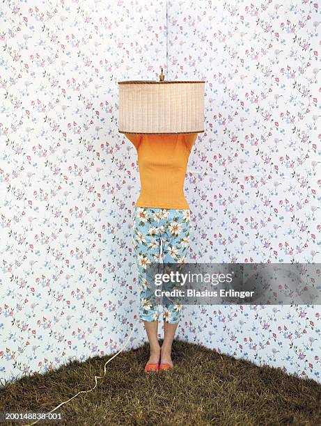 teenage girl (14-16) standing in corner with lamp shade on head - floral pattern pants stockfoto's en -beelden