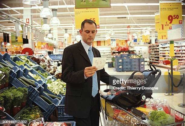 father feeding baby daughter (12-15 months) in supermarket - shopping list trolley stock pictures, royalty-free photos & images